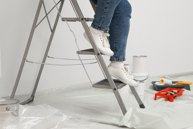 Photo of Woman climbing down metallic folding ladder near painting tools indoors, closeup