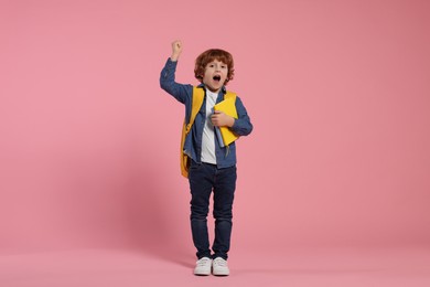 Photo of Emotional schoolboy with backpack and books on pink background