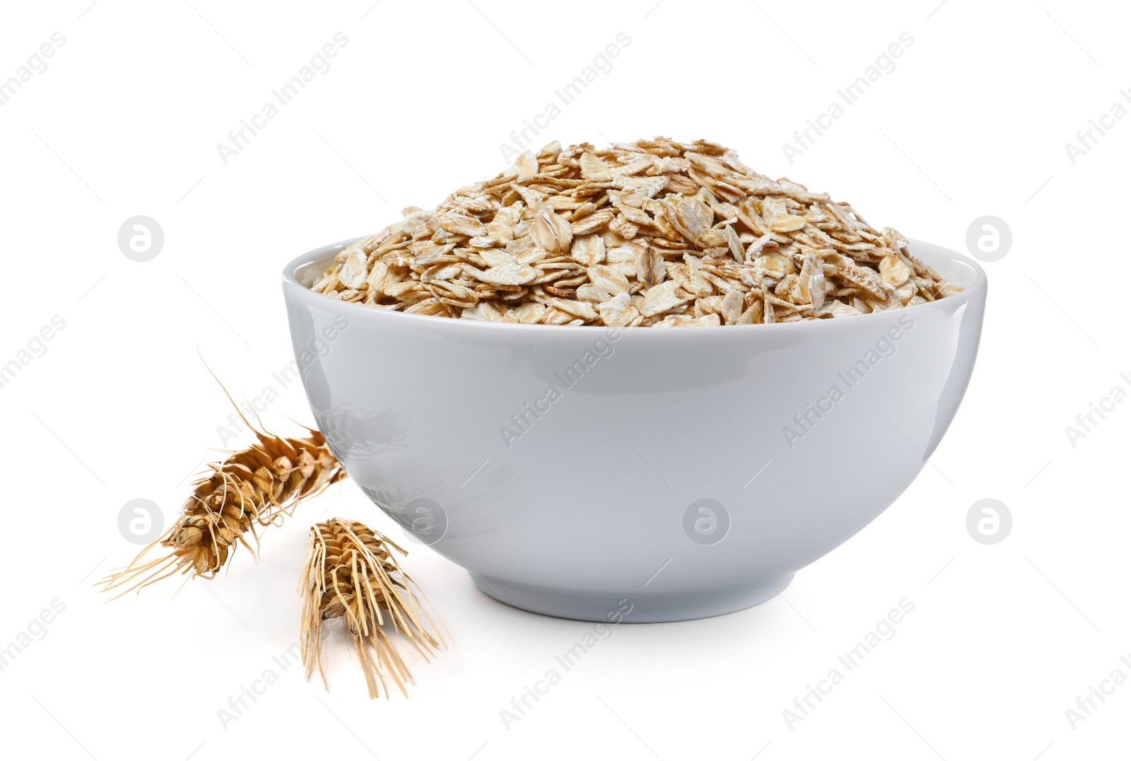 Photo of Raw oatmeal in bowl and spikelets on white background