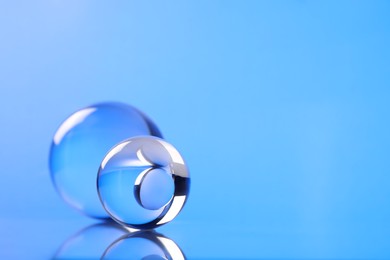 Transparent glass balls on mirror surface against blue background. Space for text