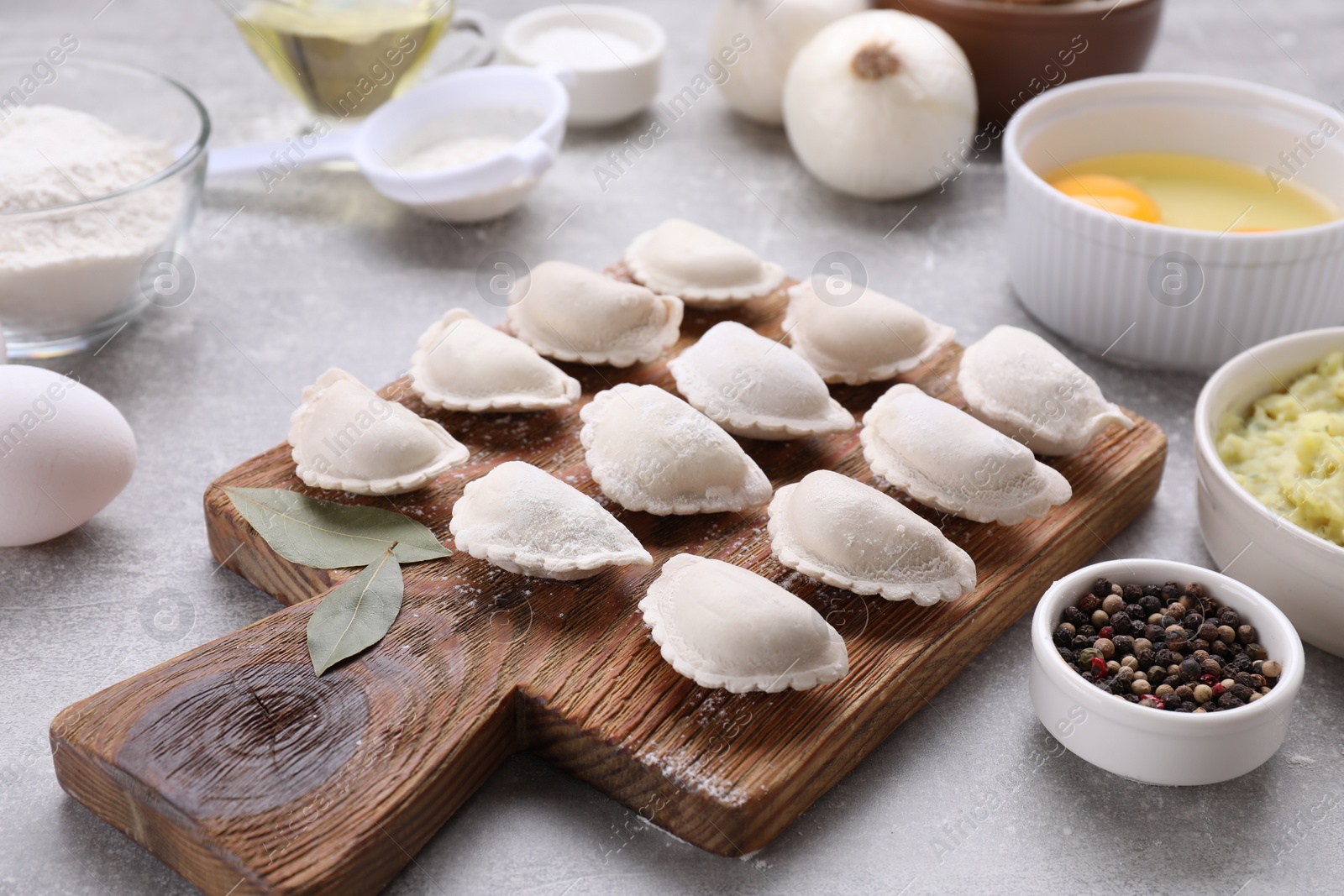 Photo of Raw dumplings (varenyky) and ingredients on grey table