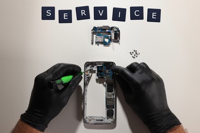 Technician repairing broken smartphone at white table, top view