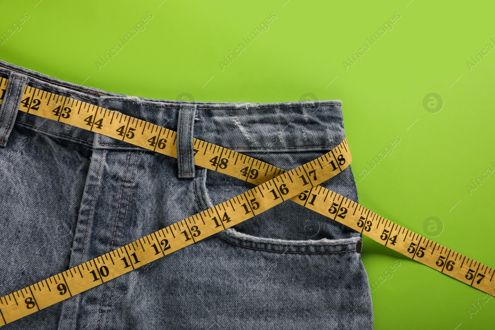 Photo of Jeans with measuring tape on green background, top view. Weight loss concept