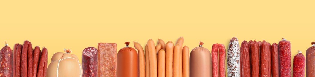 Image of Many different tasty sausages on yellow background, flat lay. Banner design