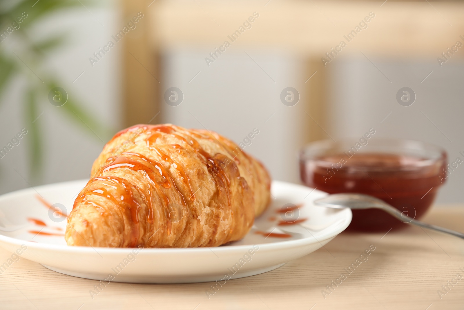 Photo of Plate of fresh croissant served with jam on wooden table indoors, closeup. French pastry