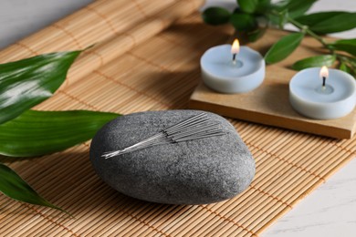 Photo of Stone with acupuncture needles and burning candles on table