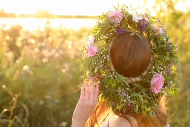 Photo of Young woman wearing wreath made of beautiful flowers outdoors on sunny day