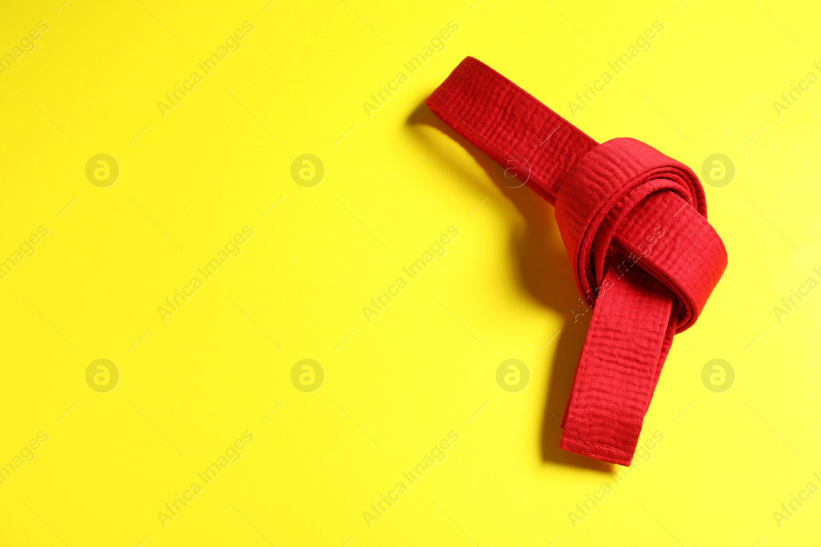 Photo of Red karate belt on yellow background, top view. Space for text