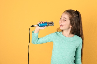 Cute girl singing in microphone on color background