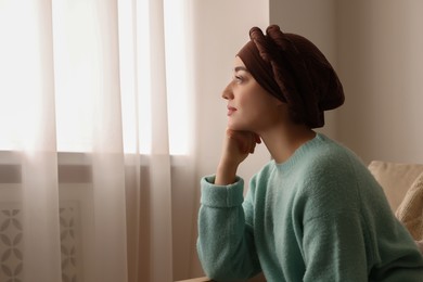 Photo of Cancer patient. Young woman with headscarf near window indoors, space for text