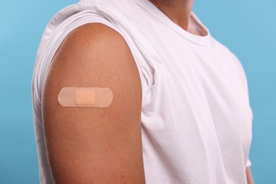 Man with sticking plaster on arm after vaccination against light blue background, closeup