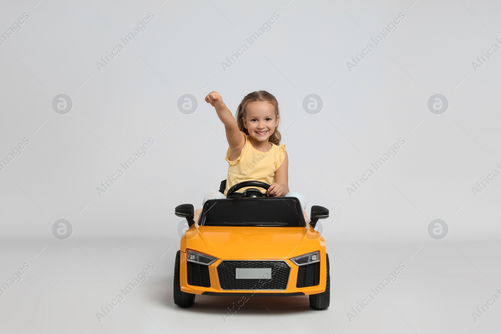 Photo of Cute little girl driving children's electric toy car on grey background