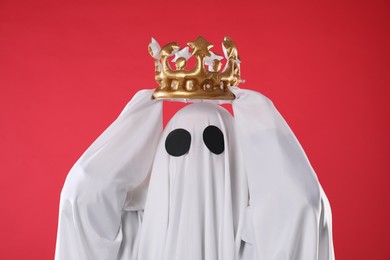 Person in ghost costume wearing luxurious crown on red background