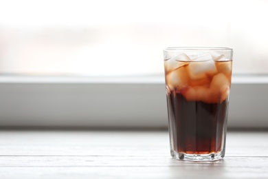 Glass of cola with ice near window, space for text