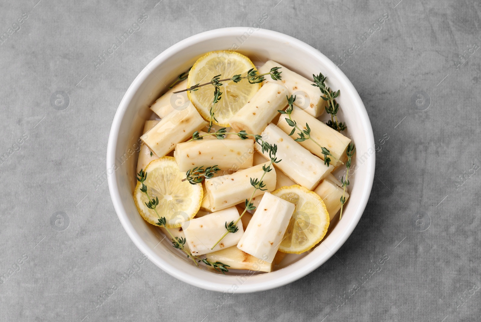 Photo of Dish with raw salsify roots, lemon and thyme on light grey table, top view