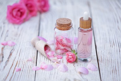 Photo of Rose essential oil and flowers on white wooden table