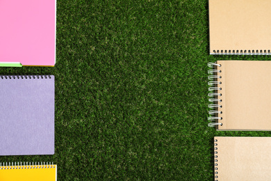 Flat lay composition with plastic and paper notebooks on green grass, space for text. Recycling concept