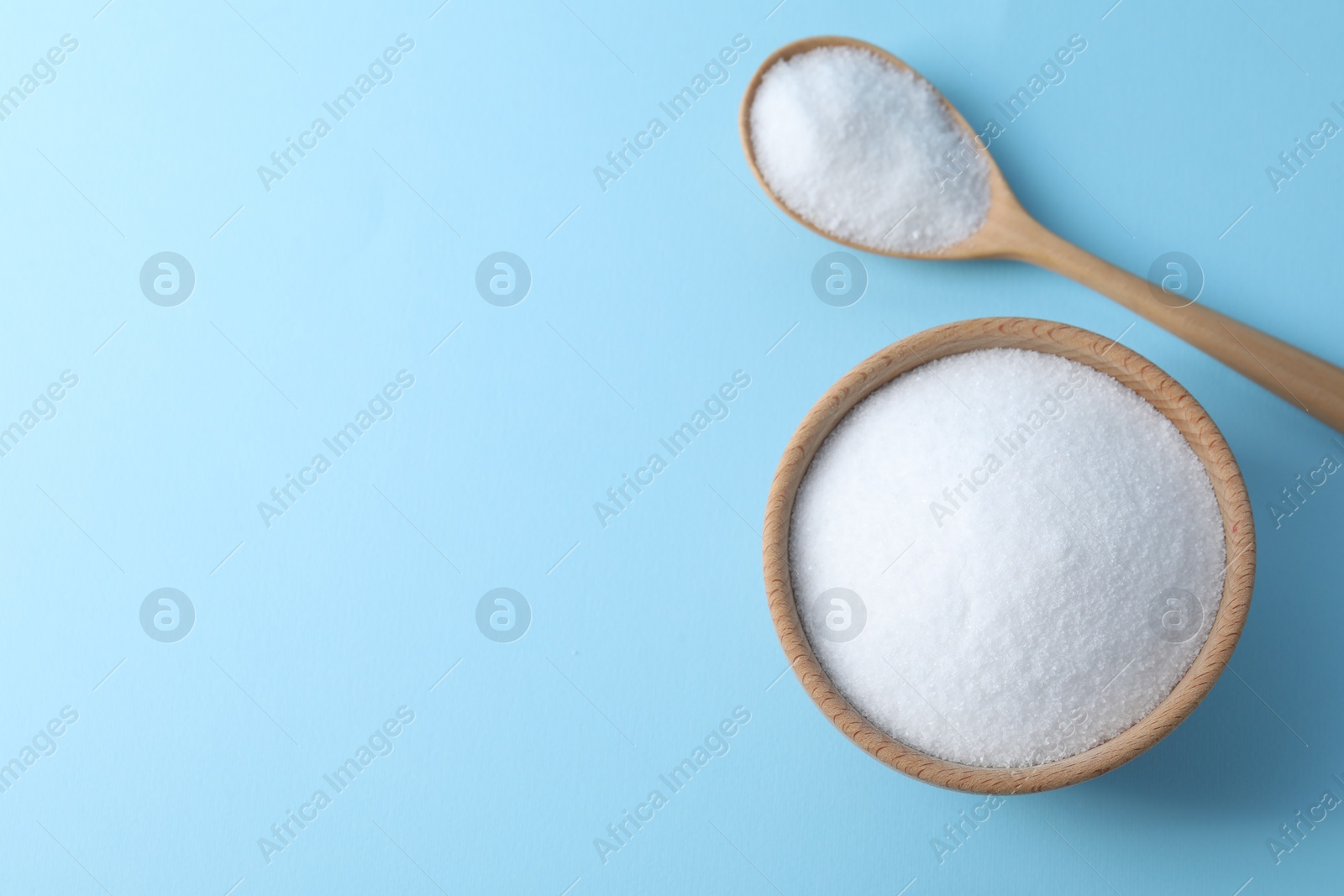 Photo of Organic white salt in bowl and spoon on light blue background, top view. Space for text