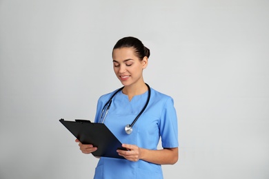Portrait of young medical assistant with stethoscope and clipboard on color background
