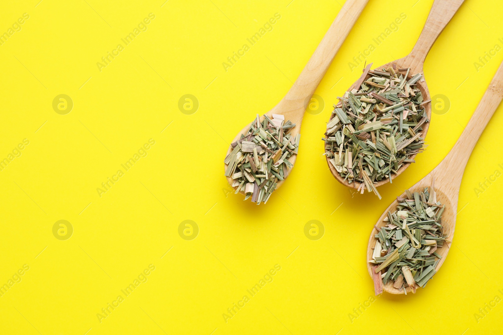 Photo of Wooden spoons with aromatic dried lemongrass on yellow background, flat lay. Space for text