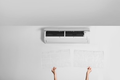 Photo of Woman holding filters under air conditioner indoors, closeup