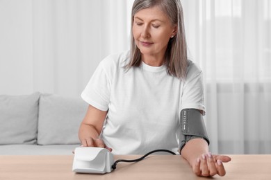 Photo of Woman measuring blood pressure at wooden table in room