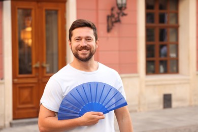 Photo of Happy man holding hand fan on city street, space for text