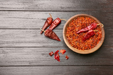Photo of Dry chili peppers and plate with flakes on wooden background, top view