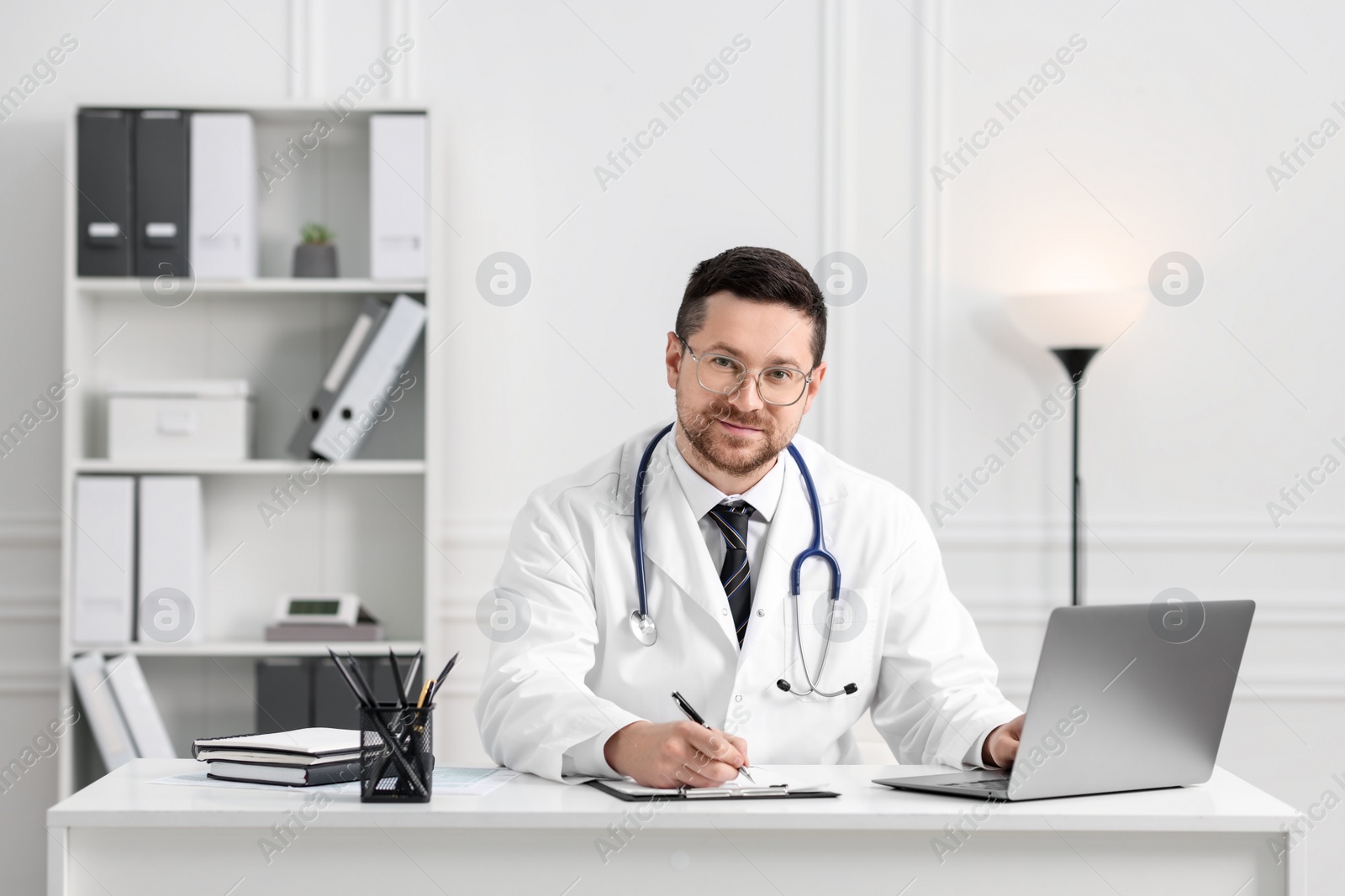 Photo of Doctor with laptop at table in clinic. Online consultation