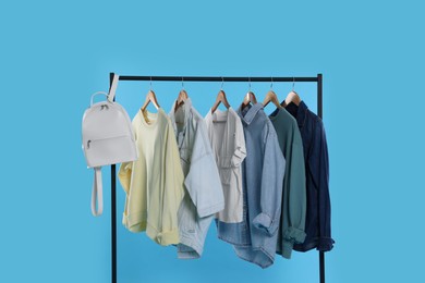 Rack with bag and stylish clothes on wooden hangers against light blue background