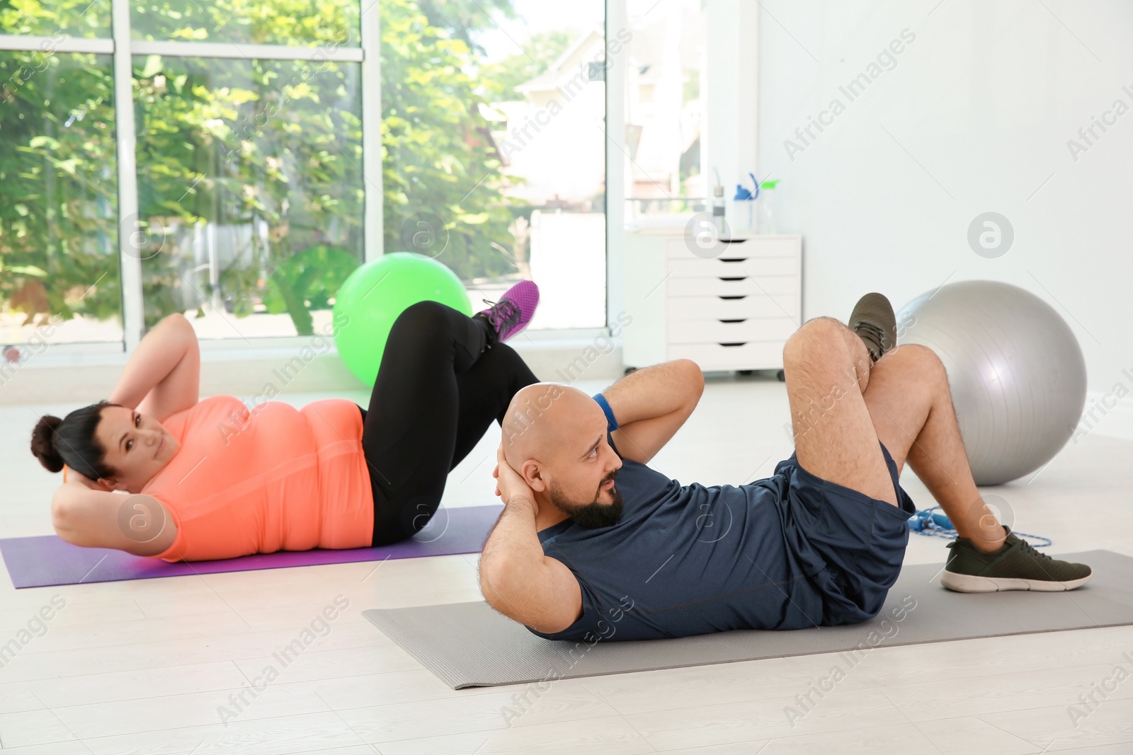 Photo of Overweight man and woman doing exercise on mats in gym