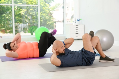 Overweight man and woman doing exercise on mats in gym