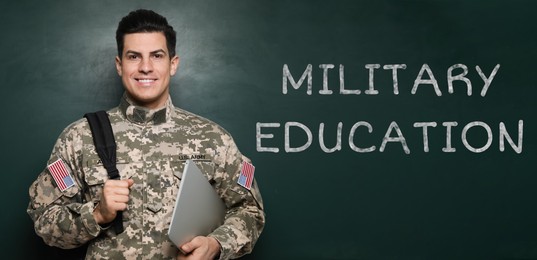 Military education. Cadet with backpack and laptop near green chalkboard