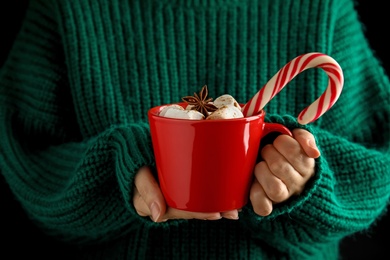 Photo of Woman holding cup of tasty cocoa with marshmallows and Christmas candy cane, closeup