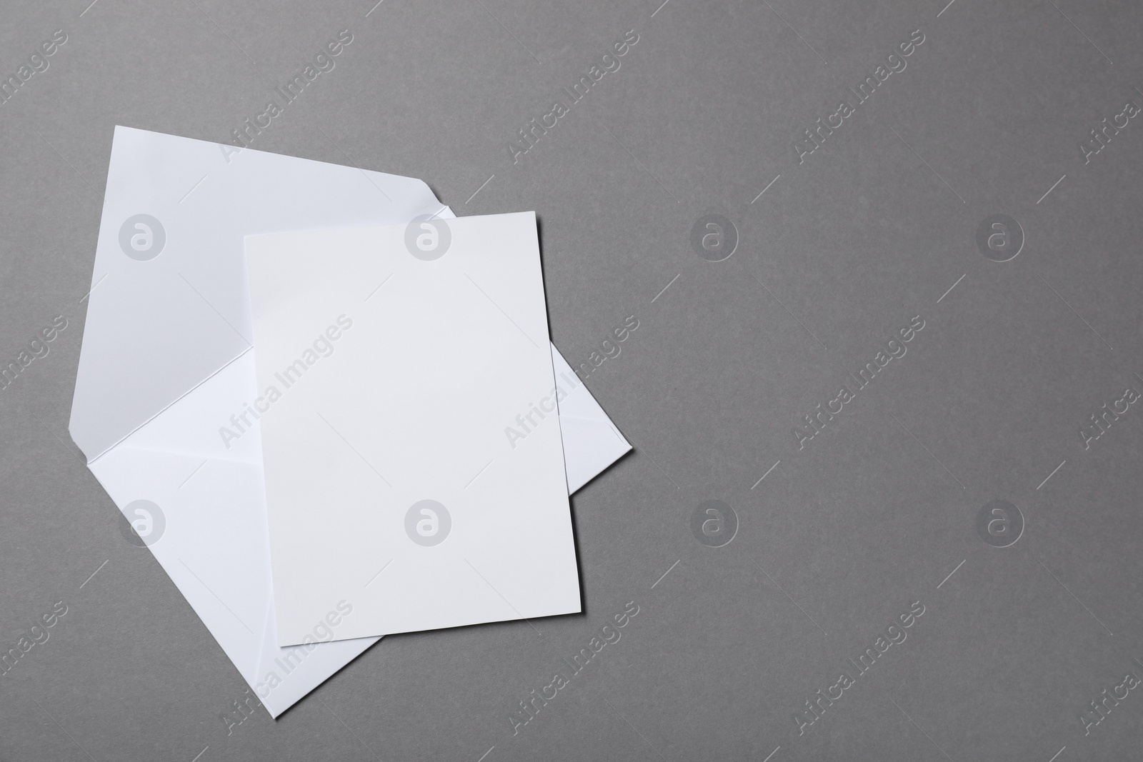 Photo of Blank sheet of paper and letter envelope on grey background, top view. Space for text