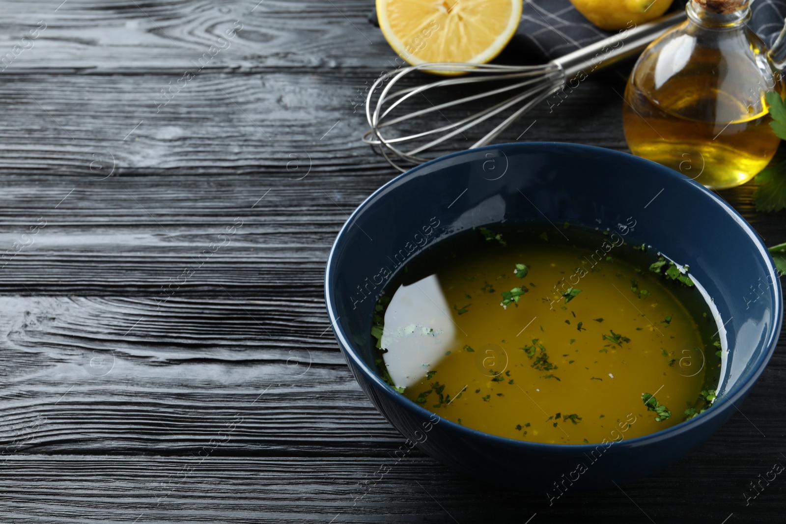 Photo of Bowl with lemon sauce on black wooden table, space for text. Delicious salad dressing