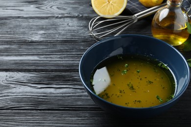 Photo of Bowl with lemon sauce on black wooden table, space for text. Delicious salad dressing