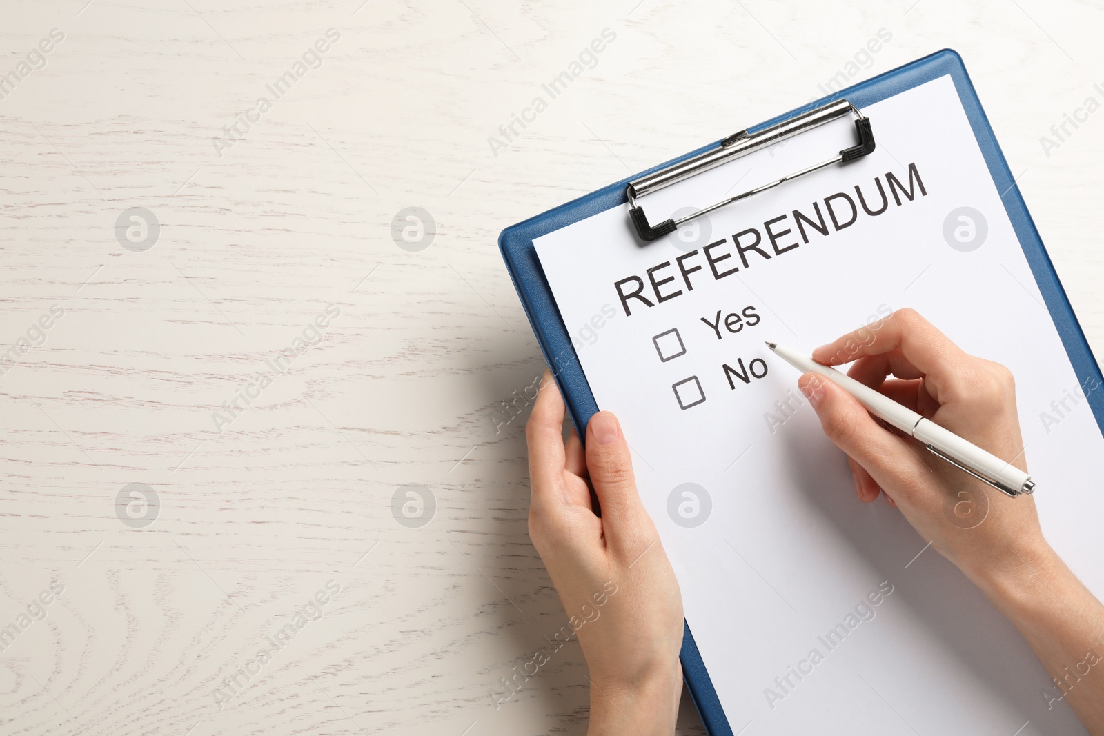 Photo of Woman with referendum ballot making decision at white wooden table, closeup. Space for text