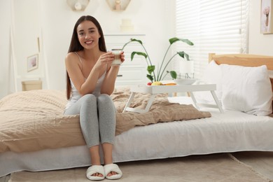 Photo of Happy young woman having breakfast near white tray on bed at home
