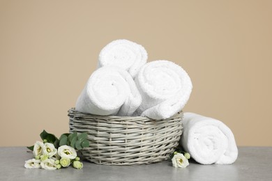 Photo of Soft rolled towels in wicker basket on grey table