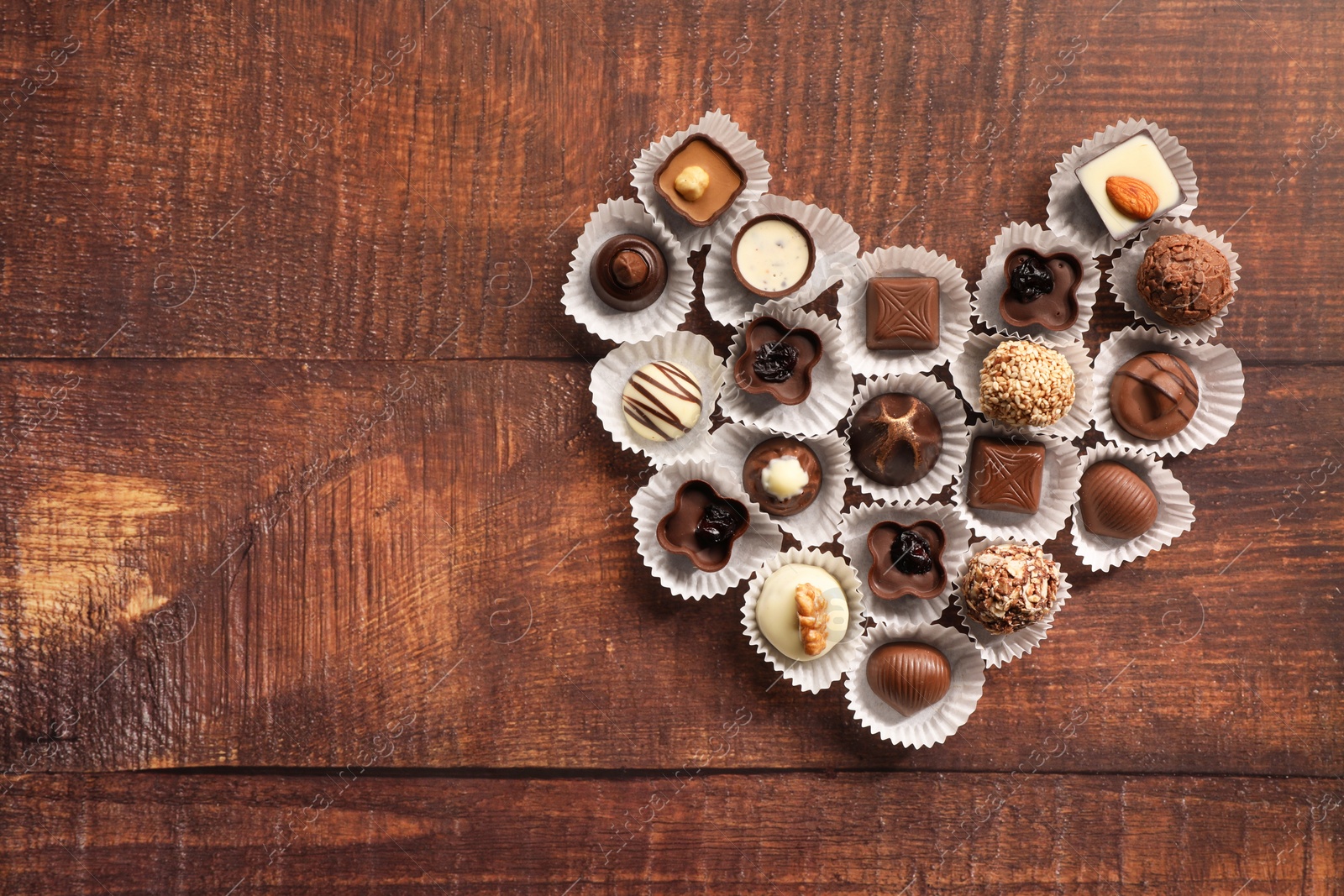 Photo of Heart made with delicious chocolate candies on wooden table, top view. Space for text