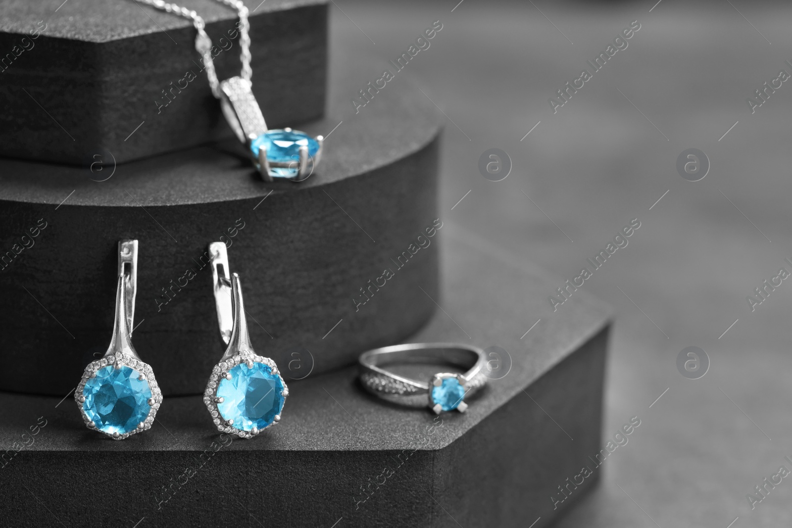 Photo of Beautiful jewelry with light blue gemstones on black podiums, space for text