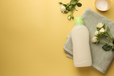 Photo of Bottle of fabric softener, towel, detergent powder and roses on pale yellow background, flat lay. Space for text