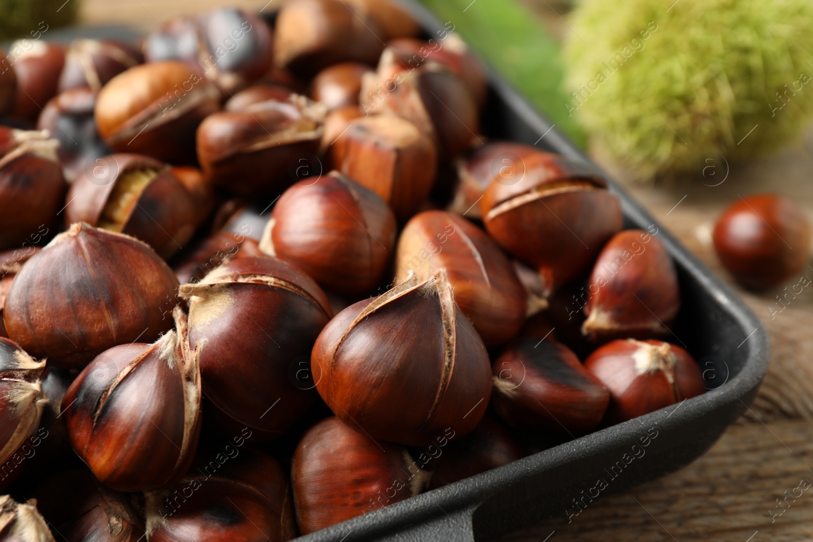 Photo of Delicious roasted edible chestnuts in baking dish on wooden table, closeup