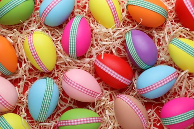 Photo of Festively decorated Easter eggs in paper filler on red background, flat lay