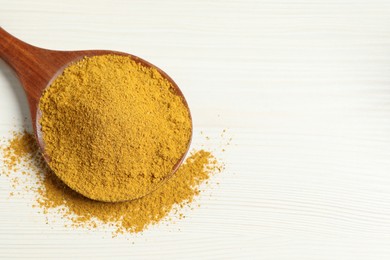 Photo of Curry powder in spoon on white wooden table, top view. Space for text