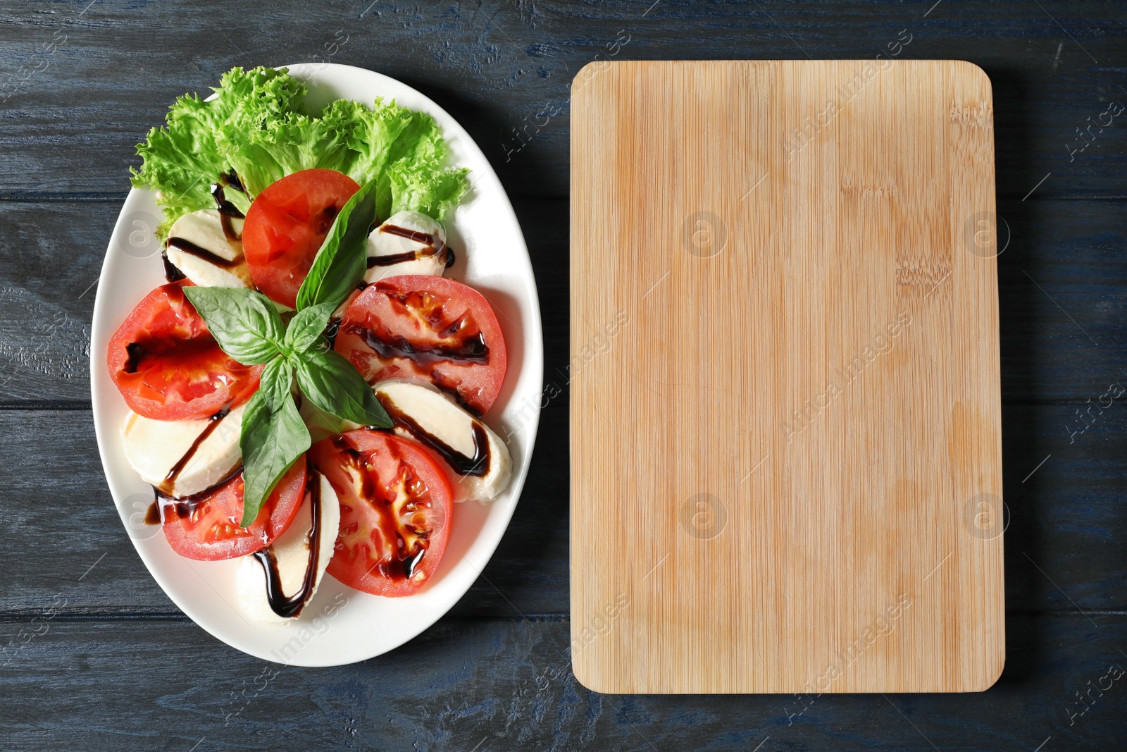 Photo of Plate with delicious fresh salad and wooden board on table, top view