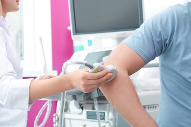 Doctor conducting ultrasound examination of elbow joint in clinic, closeup