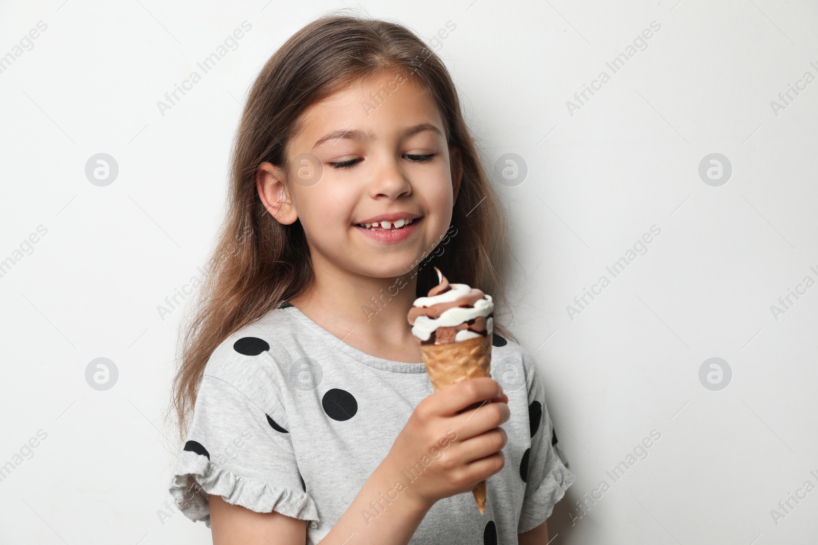 Photo of Adorable little girl with delicious ice cream against light background