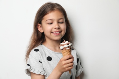 Adorable little girl with delicious ice cream against light background